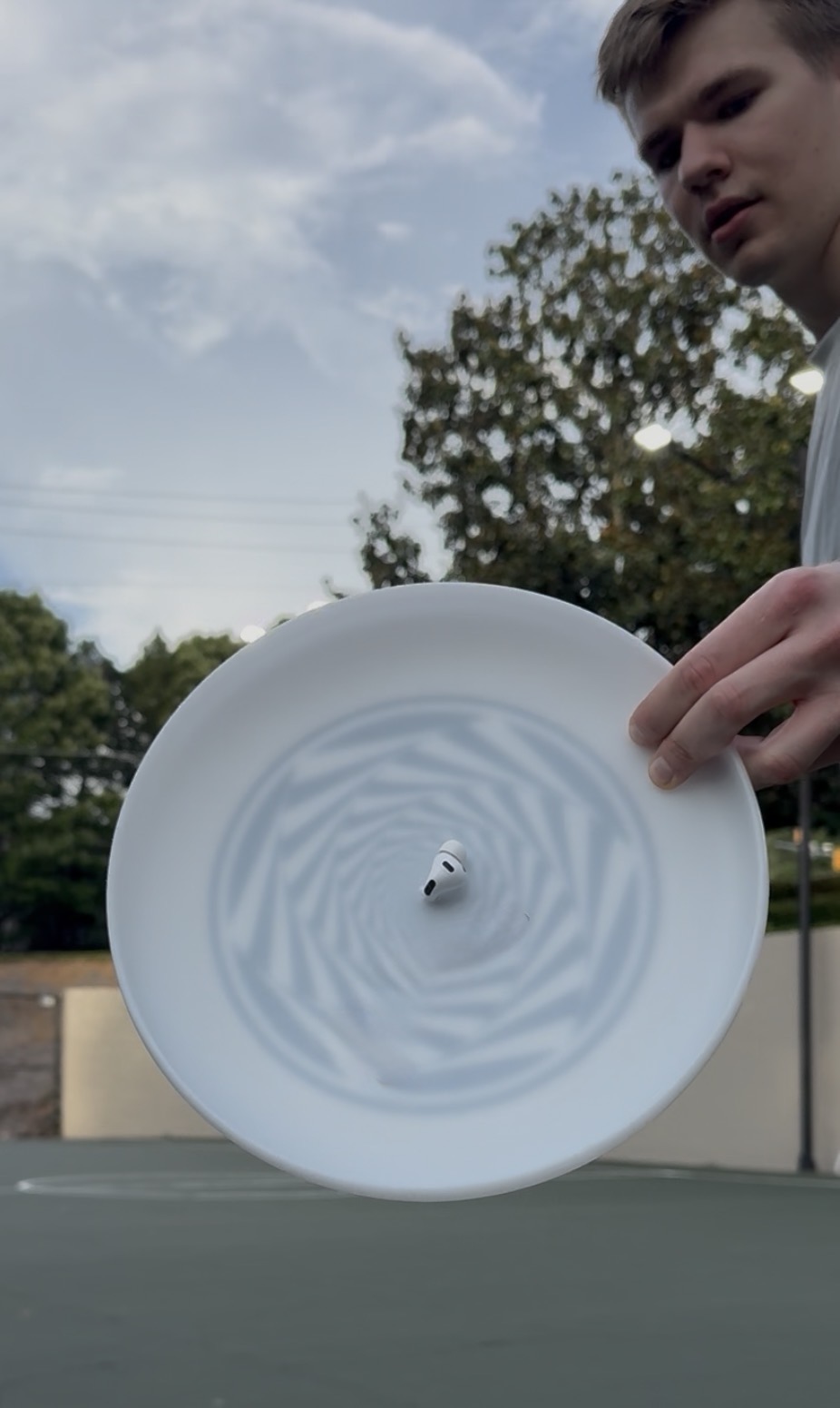 An AirPod Pro mounted in the exact centre of a flying disc, spinning as it is thrown